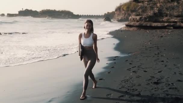 Happy nainen urheiluvaatteet kävelee pitkin mustaa hiekkarantaa, hymyilee, kääntyy ympäri
 - Materiaali, video