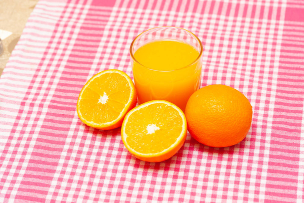 Een glas vers sinaasappelsap en sinaasappels op tafel - Foto, afbeelding