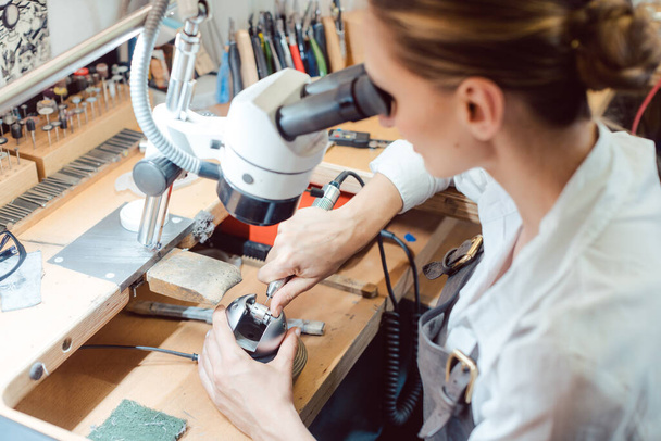 Joyero diligente trabajando en microscopio en su banco de trabajo - Foto, Imagen