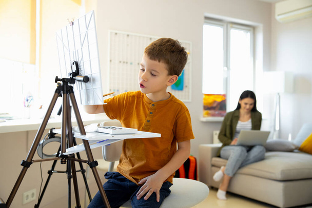 Cute little boy painting picture on easel at home - Valokuva, kuva