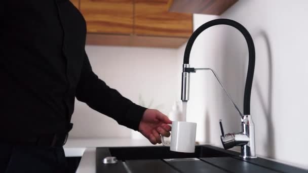 Videó folyamat férfi fekete ingben fog fehér csésze és kapcsolja be a csapot. Öntök bele egy kis vizet és hagyom, hogy lefolyjon a víz.. - Felvétel, videó