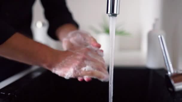 Seitenansicht und Großaufnahme eines Mannes, der sich die Hände mit Seife über dem Waschbecken wäscht. Finger und Handflächen reinigen. Wasser strömt aus dem Wasserhahn in die Spüle in der Küche. Pflege und Schutz der Hand. - Filmmaterial, Video