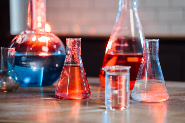 frascos y tubos de ensayo de diferentes tamaños están sobre la mesa en el laboratorio. Se llenan de líquidos azules, rojos y claros y se resaltan con luz
. - Foto, Imagen