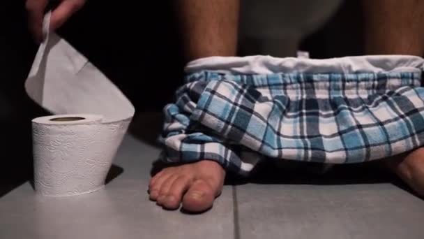 Proces wideo człowieka ręka sięgająca do rolki papieru toaletowego po defekacji i wyciąć go. Facet siedzi na trawce w pokoju odpoczynku ze spodniami na nogach. Samotny w wc lub WC. Zamknij się.. - Materiał filmowy, wideo
