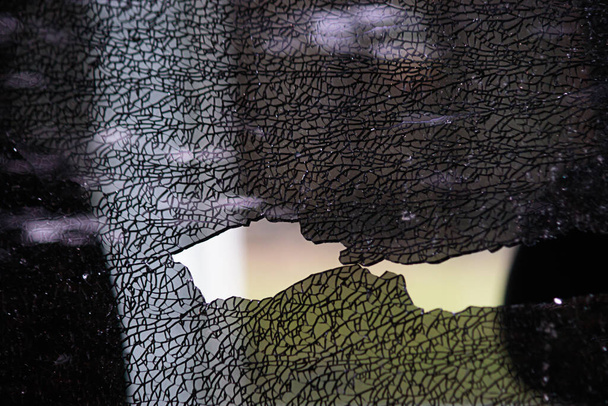 verbrijzeld glas van een autoraam dat wordt verplaatst met een zwarte handschoen - Foto, afbeelding