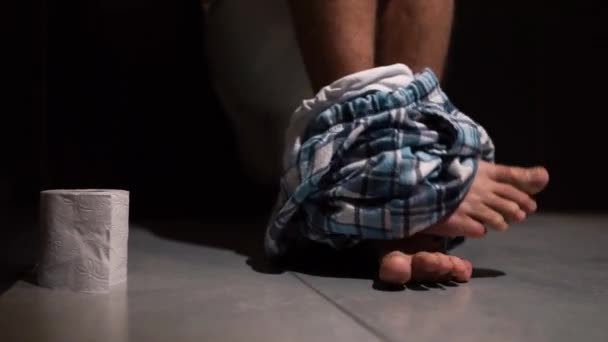 Man in rustruimte zittend op wiet tijdens hard pijnlijk ontlasting proces met broek aan zijn voeten. Na het afwerken hand reiken naar papier rol. - Video