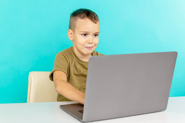 Dzieciak uczy się online w domu na laptopie w niebieskim pokoju. - Zdjęcie, obraz