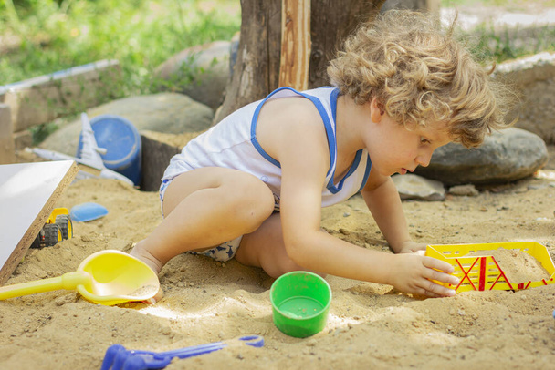 Dziecko bawi się w piaskownicy. Mały chłopiec gra na podwórku - Zdjęcie, obraz