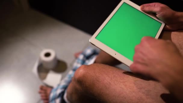 Video del hombre sentado en el inodoro o la olla y mantenga la tableta con pantalla verde en las manos. Bajando varias veces. Rollo de papel higiénico en el suelo
. - Metraje, vídeo