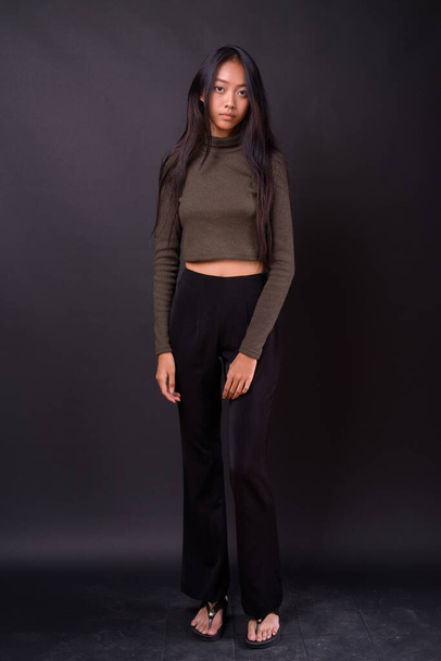 Studio shot of young beautiful Asian woman wearing turtleneck sweater against black background - Foto, afbeelding