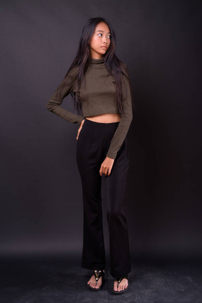 Studio shot of young beautiful Asian woman wearing turtleneck sweater against black background - Фото, изображение