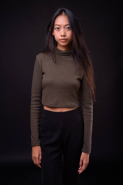 Studio shot of young beautiful Asian woman wearing turtleneck sweater against black background - 写真・画像