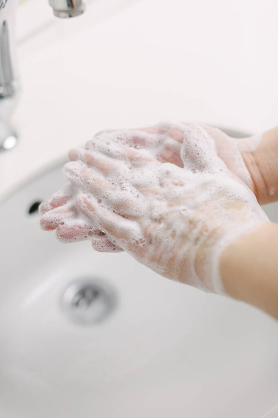 A nő kezet mos sebészi kézmosással. Legalább 20 másodpercig mossa a kezét. Dörzsöli a tenyerét. Kezet mos, hogy megvédje Covid-19-től.. - Fotó, kép
