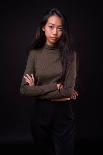 Studio colpo di giovane bella donna asiatica che indossa maglione dolcevita contro sfondo nero - Foto, immagini