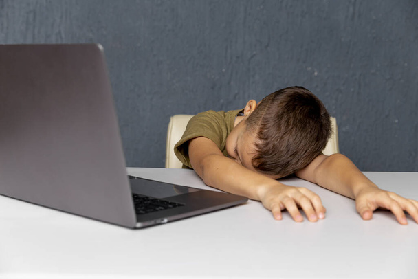 Yurt içi eğitim. Yorgun çocuk dizüstü bilgisayarın önünde oturuyor.. - Fotoğraf, Görsel