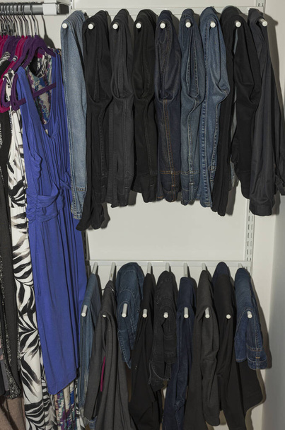 Close up view of interior of built-in wardrobe. Blue and black jeans on white hangers. Cloth organizer.  - Photo, Image