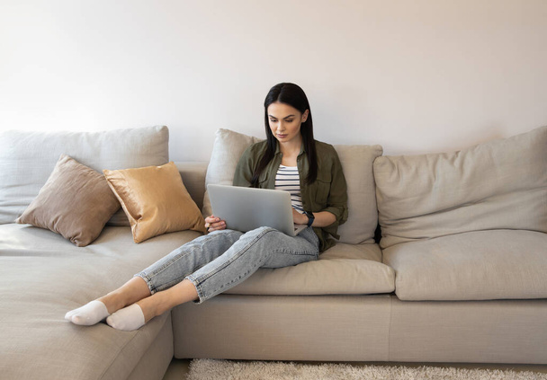 Serious young woman sitting on the sofa with modern device stock photo - Φωτογραφία, εικόνα