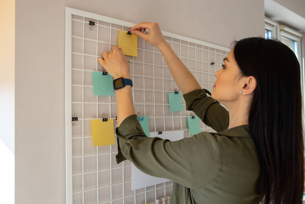 Woman sticking notes on the metal board stock photo - Фото, изображение