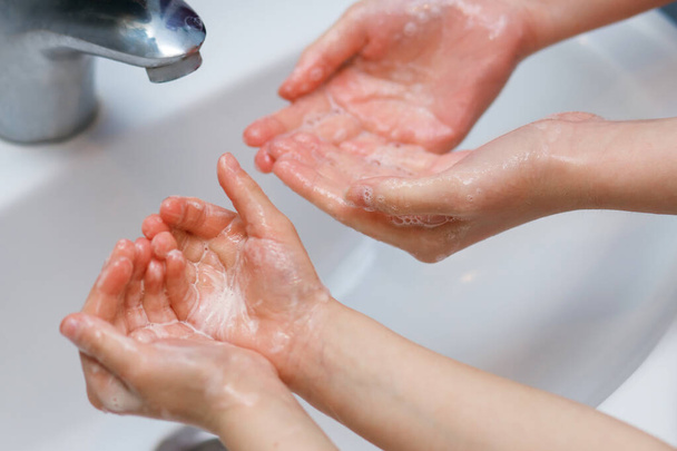 Δύο παιδιά, δύο αδελφές πλένουν τα χέρια τους με σαπούνι στο νεροχύτη, προστατευμένα από ιογενή λοίμωξη, προστασία από ιούς Covid 19, υγειονομική περίθαλψη, προστασία από τον κορωνοϊό, καθαρισμό δέρματος - Φωτογραφία, εικόνα