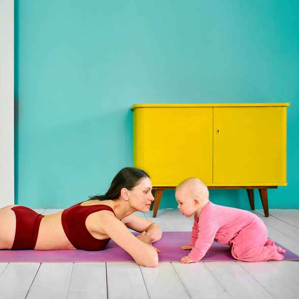 young girl practicing yoga at home with a small child - Valokuva, kuva