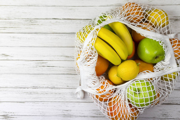 gyümölcs banán alma narancs citrom caton háló, string bevásárló táska fehér fa háttér. nulla hulladék koncepció. Műanyag nélkül. - Fotó, kép