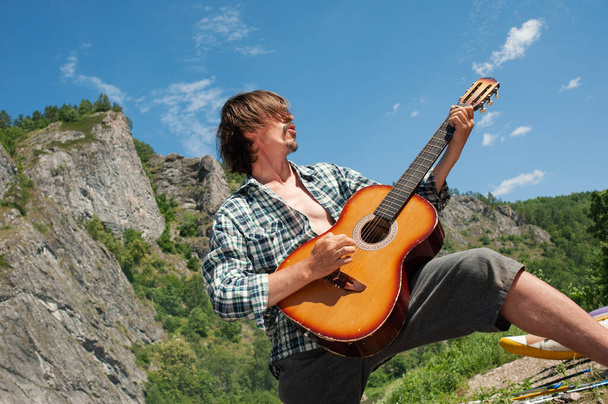 Um turista masculino toca rock roll em uma guitarra com vista para as montanhas. Desfrute de recreação ao ar livre
 - Foto, Imagem