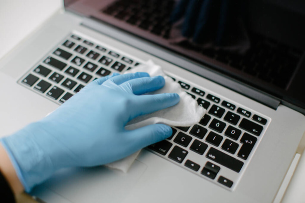 Kobieta czyści klawiaturę komputera, by chronić ją przed koronawirusem. Używa ścierki do czyszczenia i rękawicy.. - Zdjęcie, obraz