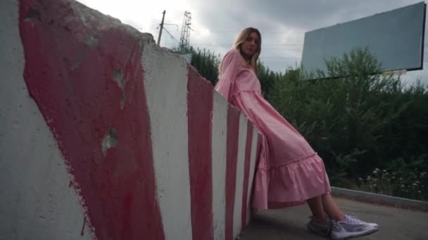 Komoly lány rózsaszín ruhában elkezd nevetni, üres hirdetőtábla a háttérben - Felvétel, videó