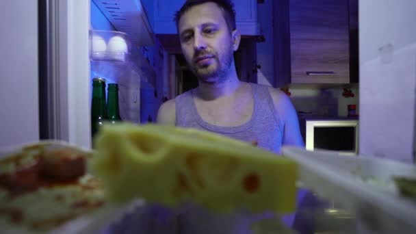 Een man tijdens de zelfisolatie is op zoek naar voedsel in de koelkast. Restvoedsel in de koelkast tijdens quarantaine. Het verbod om het huis op straat te verlaten. Blijf thuis. Coronavirus. COVID-19 - Video