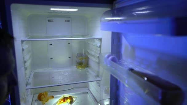 Ένας άντρας κατά τη διάρκεια της αυτο-απομόνωσης ψάχνει για φαγητό στο ψυγείο. Απομεινάρια τροφής στο ψυγείο κατά τη διάρκεια της καραντίνας. Η απαγόρευση εξόδου από το σπίτι στο δρόμο. Μείνε σπίτι. Coronavirus. COVID-19 - Πλάνα, βίντεο