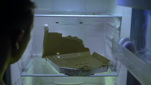 Man looking for food in the fridge. Unshaven man digs in his fridge, he takes pizza. Night hunger. Hangover. Bachelor's fridge, view from behind. Dirty fridge full of stale food. Quarantine. Observation. - Footage, Video
