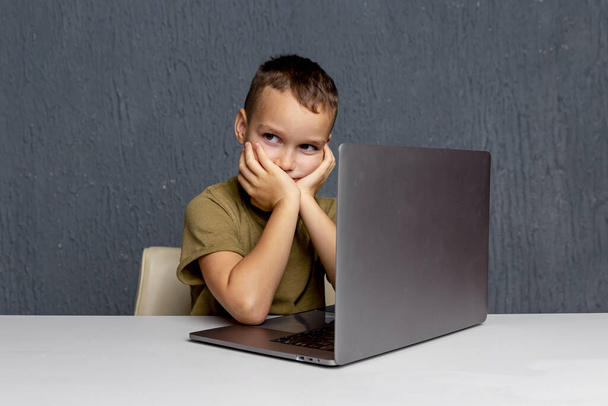 Online home learning έννοια. Αγόρι κάθεται με τον υπολογιστή και κάνει την εργασία. - Φωτογραφία, εικόνα