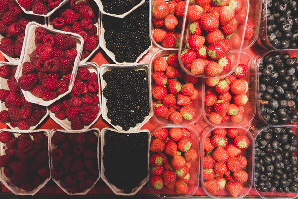 Array von Schalen oder Schalen mit saftigen Himbeeren, Brombeeren, Erdbeeren und Blaubeeren auf einem lokalen Wochenmarkt in Stockholm - Foto, Bild
