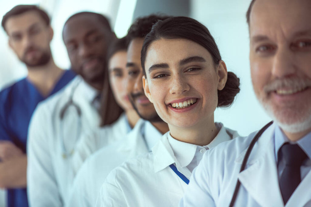 Cheerful female doctor standing with colleagues in clinic - Photo, image