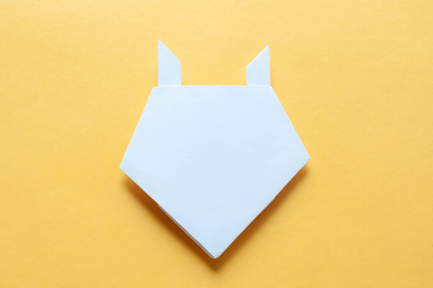 Step 17. Hands of a child on a yellow background divide a square of white paper into triangles. Origami bull concept. - Valokuva, kuva