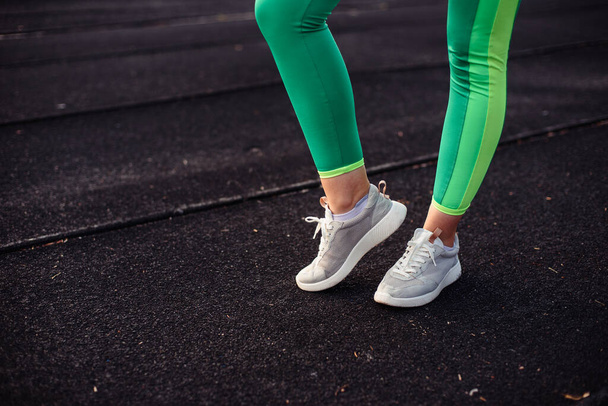 Ноги девушки в светло-зеленых леггинсах на тренировке на стадионе, на улице
 - Фото, изображение
