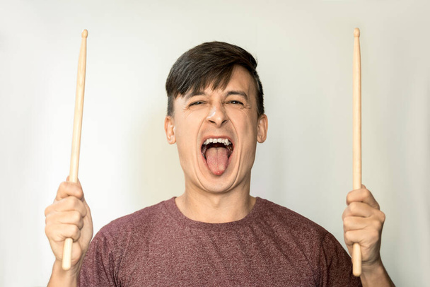 Portrait of a young man with dark hair, on a light background with drumsticks. - Photo, image