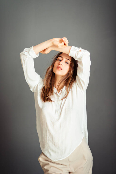 Молодая девушка в белой рубашке на сером фоне. Французская женщина в белой блузке на фоне серых стен. Без ретуши
. - Фото, изображение