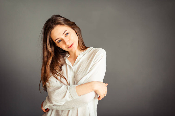 Young girl in a white shirt on a gray background. French woman in white blouse against a background of gray walls. Without retouching. - Foto, imagen