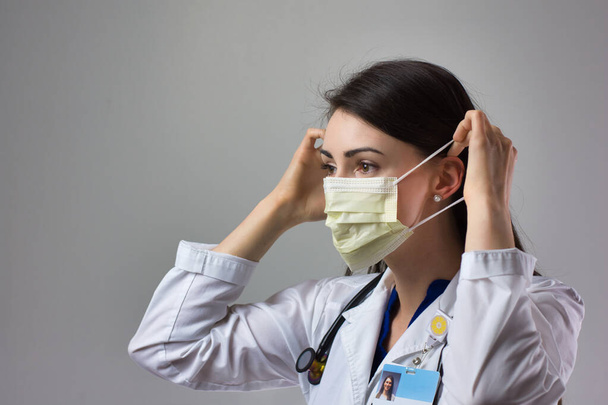 Woman healthcare professional demonstrating proper donning of mask for protection from coronavirus. Up close female healthcare worker putting on safety equipment on grey background - Фото, зображення