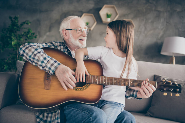 Photo of aged old grandpa little pretty granddaughter sitting comfy sofa playing guitar teaching bonding spend time together stay home quarantine safety modern interior living room indoors - Photo, image