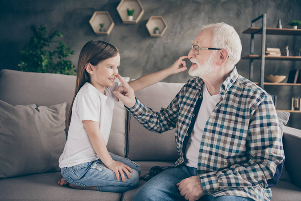 Profile photo of funny old grandpa little granddaughter sit sofa stay house quarantine safety playful good mood touch noses giggling modern interior living room indoors - Photo, Image