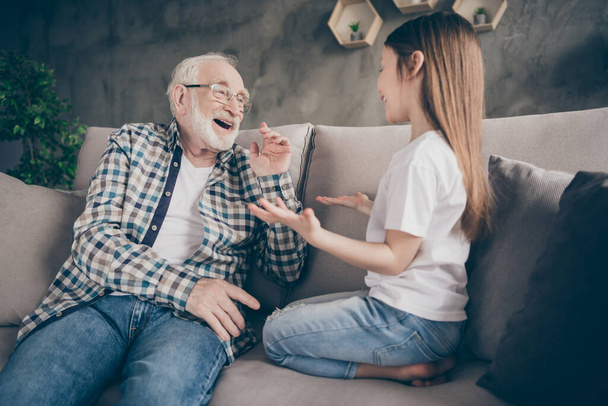 Photo of two people old grey haired grandpa little granddaughter sitting comfort sofa telling news secrets stay home house quarantine safety modern design living room indoors - Foto, imagen