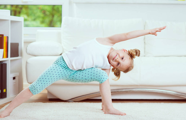 Cute little child girl making morning exercises and yoga  at home - Foto, immagini