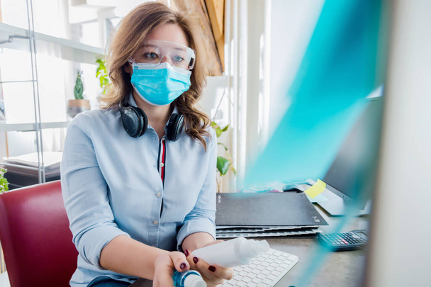 young woman in medical mask holding sanitizers and working with computer - Foto, Imagem