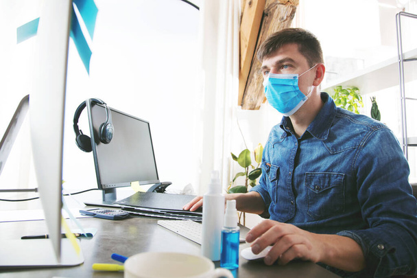 young man wearing medical mask and working with desktop computer in office - Fotoğraf, Görsel