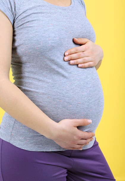 Mujer embarazada tocando su vientre sobre fondo amarillo
 - Foto, Imagen