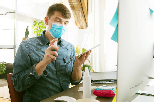 young man in medical mask cleaning computer keyboard with sanitizer - Foto, Imagen