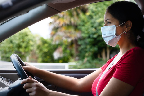 Young hispanic woman wearing face mask driving her car. Covid-19 (Corona virus) concept - Photo, image