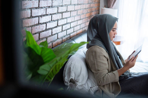 Musulmán asiático mujer usando tableta sentado en la cama
 - Foto, Imagen